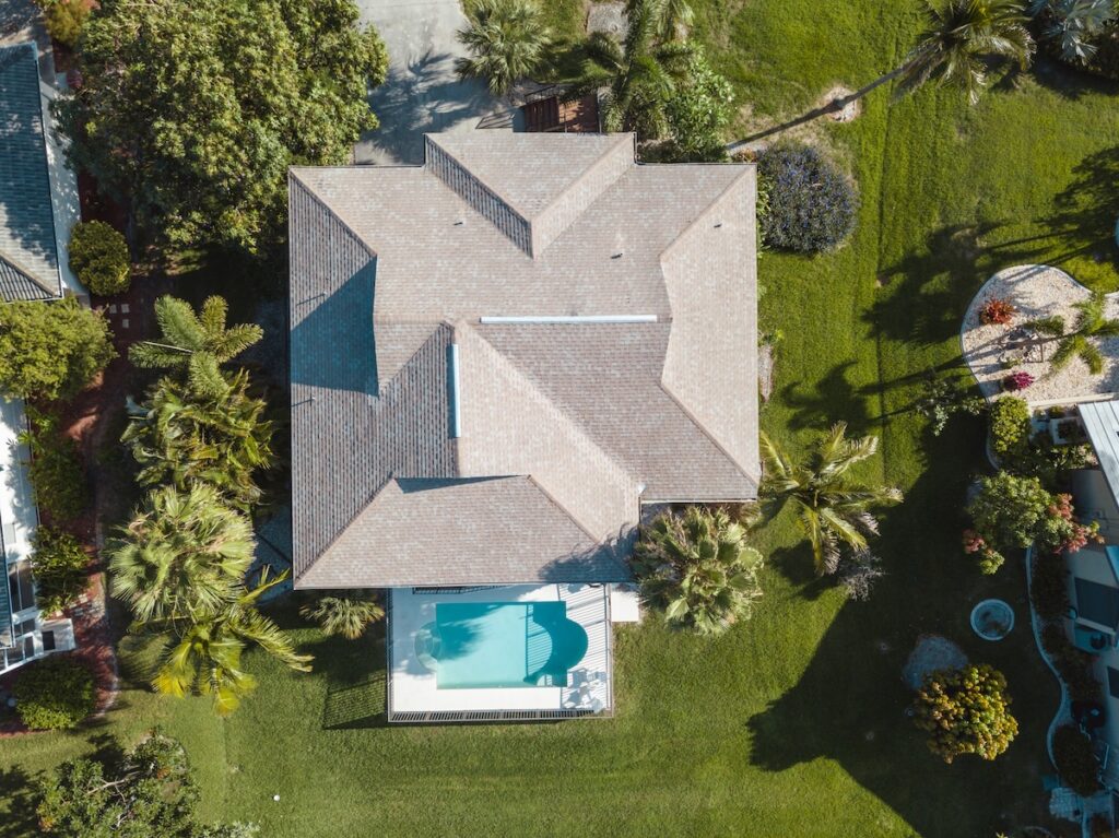 Aerial view of a residential home with asphalt roofing and a pool