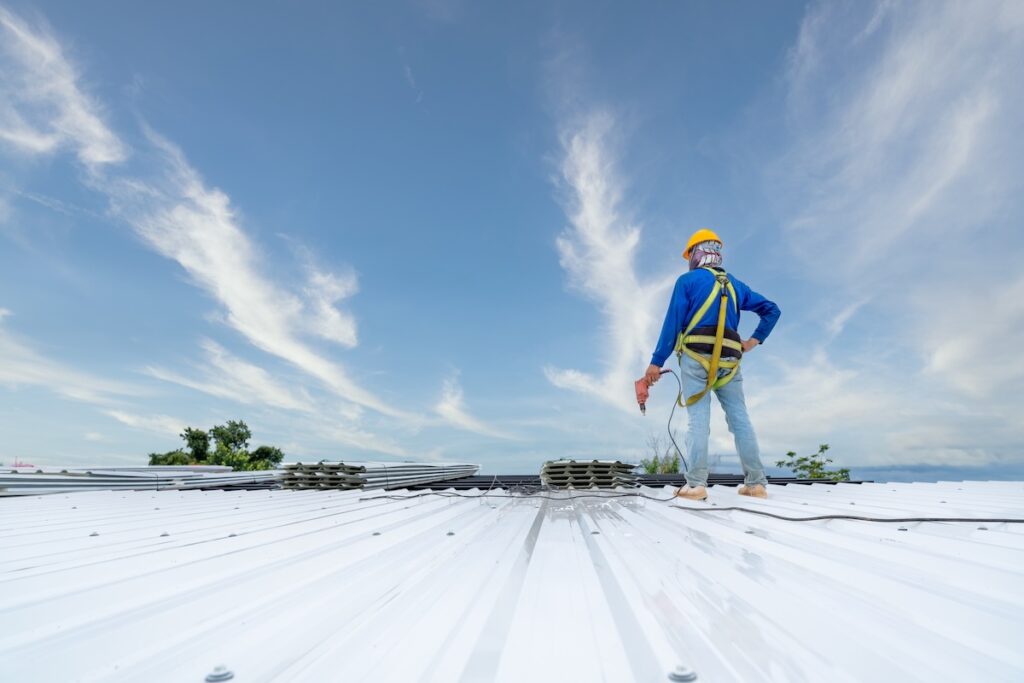 A roofer using an electric tool to secure metal commercial roofing panels