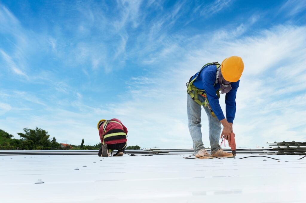 Construction worker installing new roofing with metal sheets.